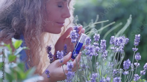 Beautiful girl sniffing roller shutter with aroma oils among greenery and lavender on a summer day. The concept of natural aromatic oils.