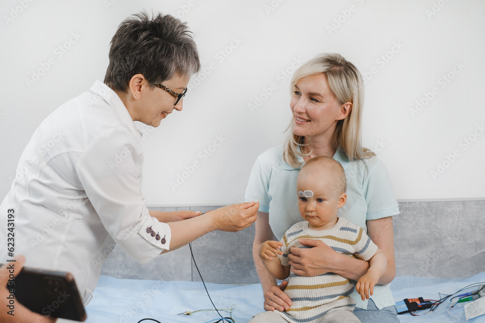 Child having hearing exam at otolaryngologist. Examining little patient, hearing test of infant kid by audiologist. Mother with baby visiting doctor for checkup Child having hearing exam at otolaryngologist. Examining little patient, hearing test of infant kid by audiologist. Mother with baby visiting doctor for checkup