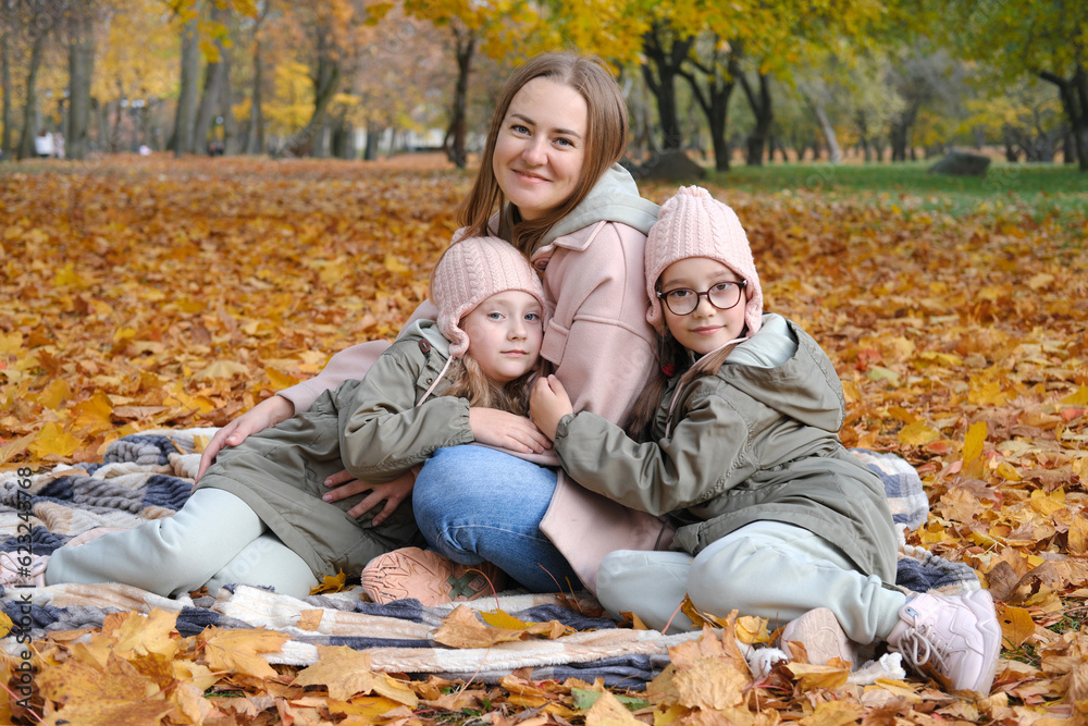 A happy mother with her twin daughters spends time sitting on a blanket in an autumn park. happy family moments A happy mother with her twin daughters spends time sitting on a blanket in an autumn park. happy family moments