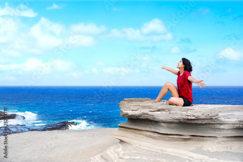 Young woman sitting on large rock cliff  by Hawaiian  ocean