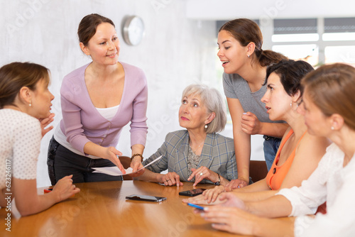 Women of different ages examine documents while sitting at table in office