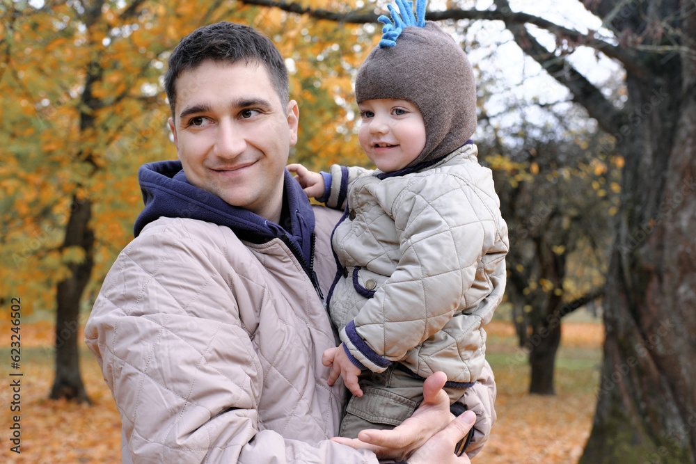 Dad and son spend time together in the autumn park. Father holding his son in his arms Dad and son spend time together in the autumn park. Father holding his son in his arms