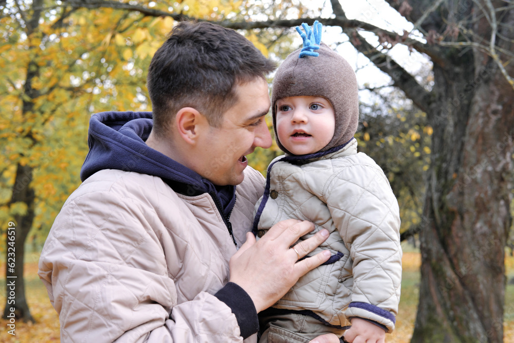 Dad and son spend time together in the autumn park. Father holding his son in his arms Dad and son spend time together in the autumn park. Father holding his son in his arms