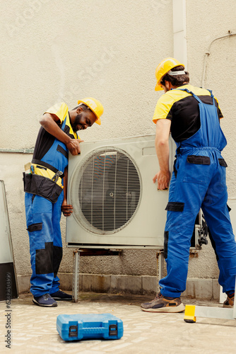 Professional worker and licensed serviceman taking apart old unfunctional condenser to replace it with new performant air conditioner after draining refrigerant and replacing ductwork photo