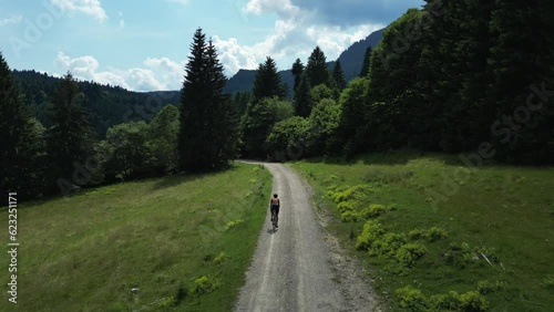Aerial drone view pro cyclist's intense gravel bike climb on a mountain trail.Cycling in nature on sunny summer day.Gravel bike adventure.Cyclist training on bicycle in mountains on gravel road.
