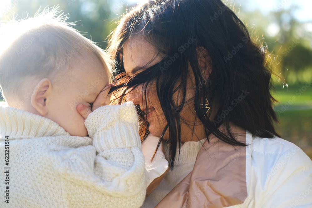 Mother and son walking in autumn park outdoor. Woman holding toddler boy on hands. Family of two