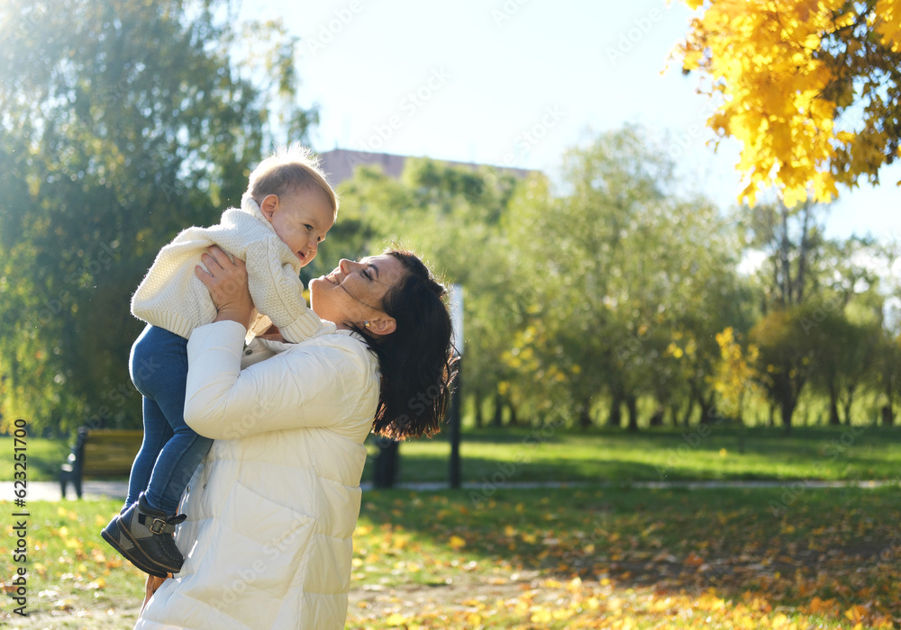 Caucasian young mother playing throwing up in air cute funny adorable toddler boy. Mom and son having fun in autumn fall park with yellow leaves. Family lifestyle activity outdoor.