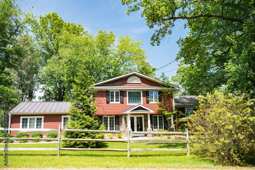 typical American two-story residential building with a well-maintained front yard and large trees in the yard. photo