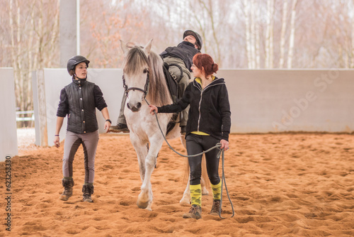 Hippotherapy assistance therapist with medical disability patient on equestrian riding hall.