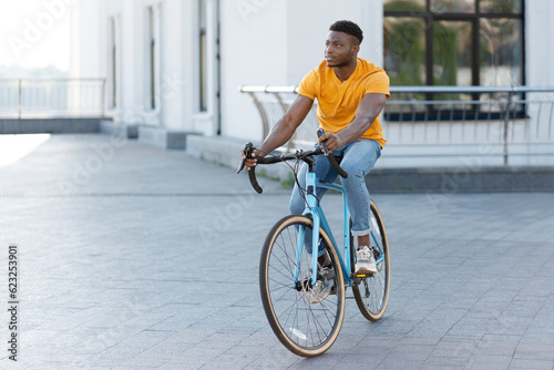 Full length view of handsome smiling African American man riding bicycle on urban street
