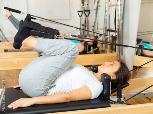 Side view of focused sportswoman stretching body on pilates chair while doing forward bends during workout