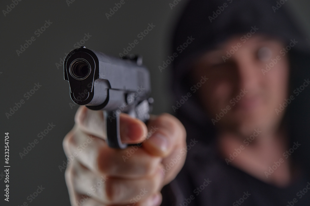 robber with gun aiming into camera. Man in hood threatens with firearm. Weapon in person's hands. Murderer or armed thief. Criminal with pistol. robber with gun aiming into camera. Man in hood threatens with firearm. Weapon in person's hands. Murderer or armed thief. Criminal with pistol.