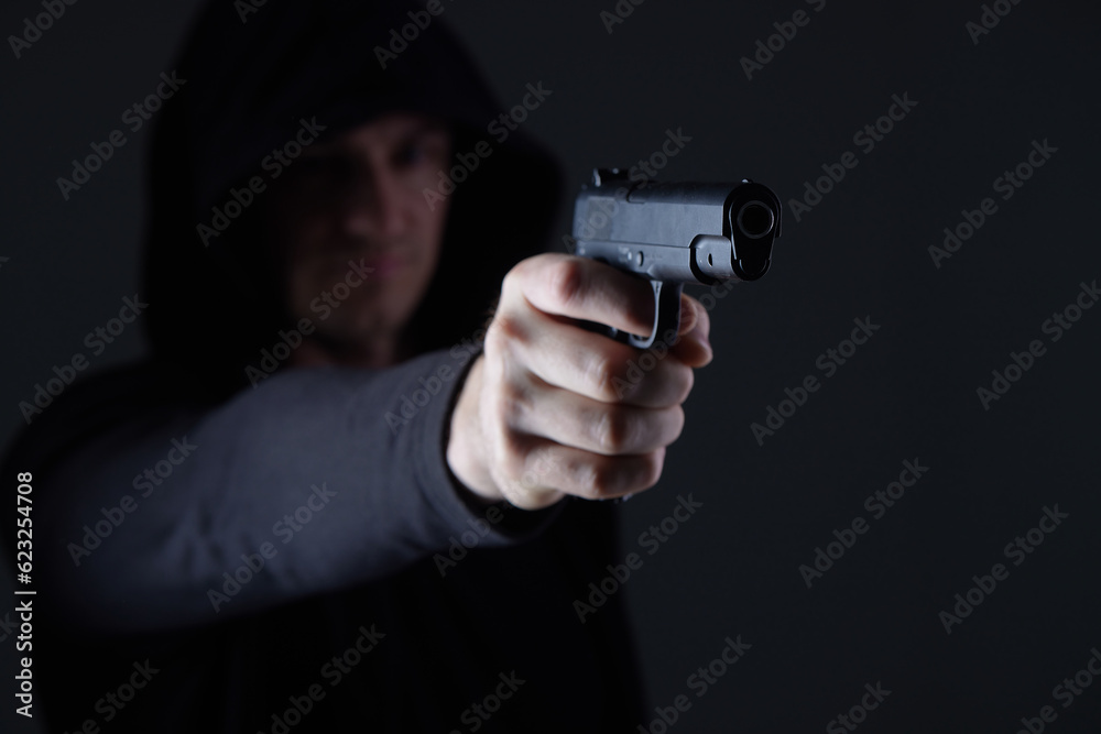 robber with gun aiming into camera. Man in hood threatens with firearm. Weapon in person's hands. Murderer or armed thief. Criminal with pistol. robber with gun aiming into camera. Man in hood threatens with firearm. Weapon in person's hands. Murderer or armed thief. Criminal with pistol.