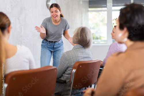 Young positive woman speaker in casual clothes gives lecture in front of audience in office