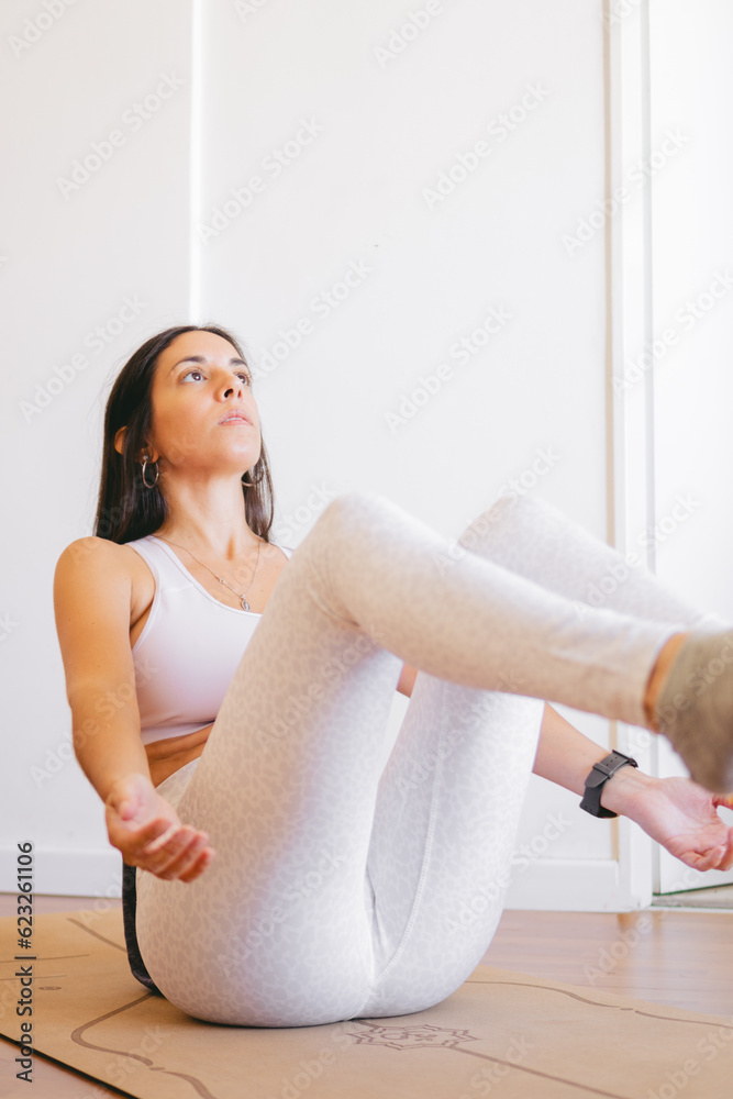 young Latin woman sitting on her yoga mat balancing with her legs and arms raised at home young Latin woman sitting on her yoga mat balancing with her legs and arms raised at home