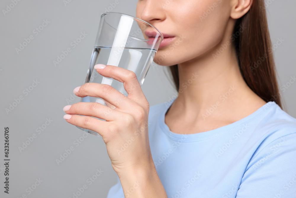 Healthy habit. Woman drinking fresh water from glass on grey background, closeup Healthy habit. Woman drinking fresh water from glass on grey background, closeup