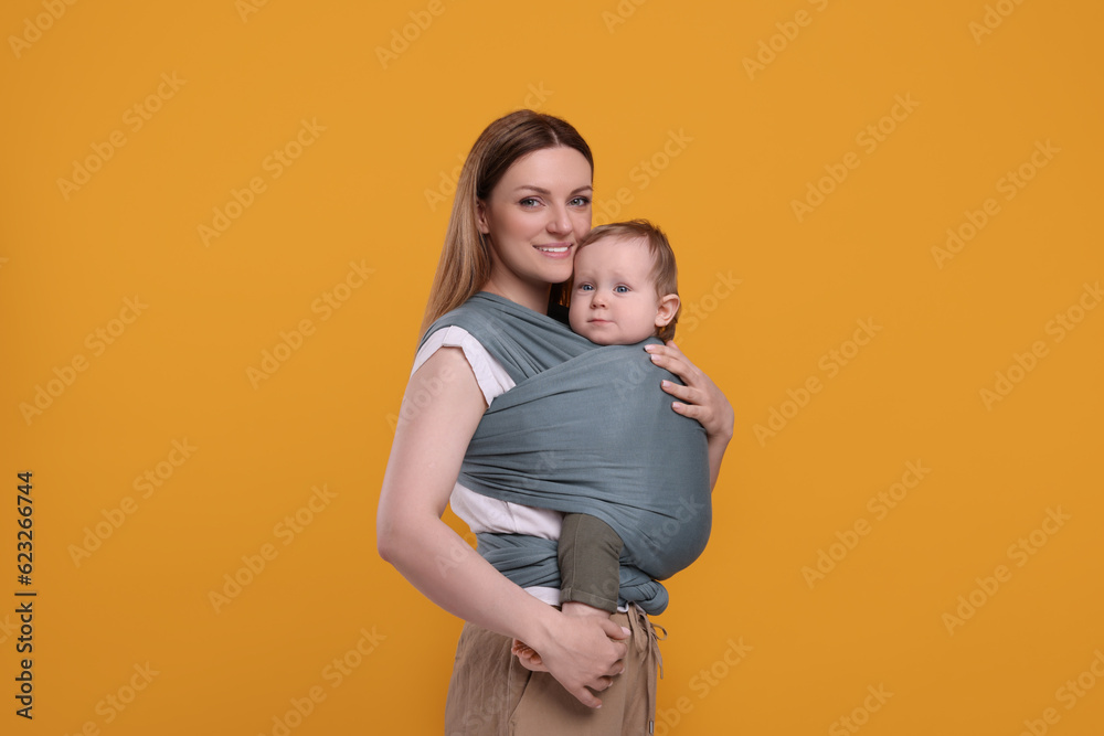 Mother holding her child in baby wrap on orange background Mother holding her child in baby wrap on orange background