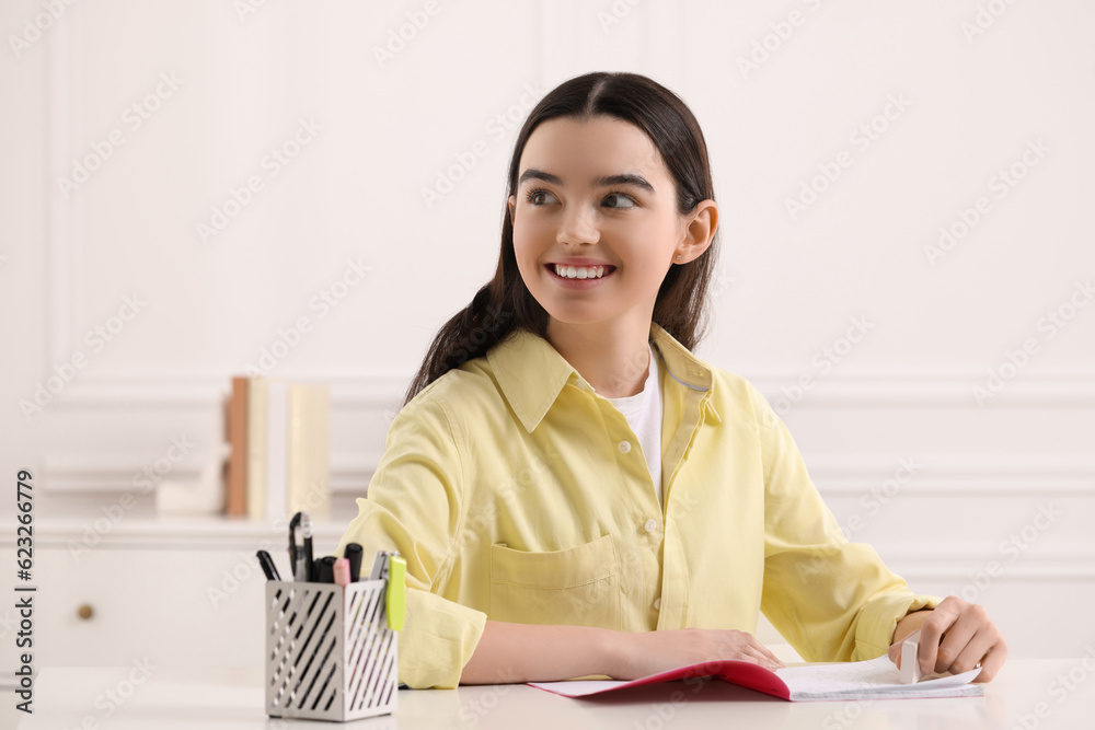 Teenage girl erasing mistake in her notebook at white desk indoors Teenage girl erasing mistake in her notebook at white desk indoors