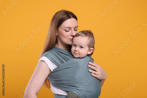 Mother holding her child in baby wrap on orange background
