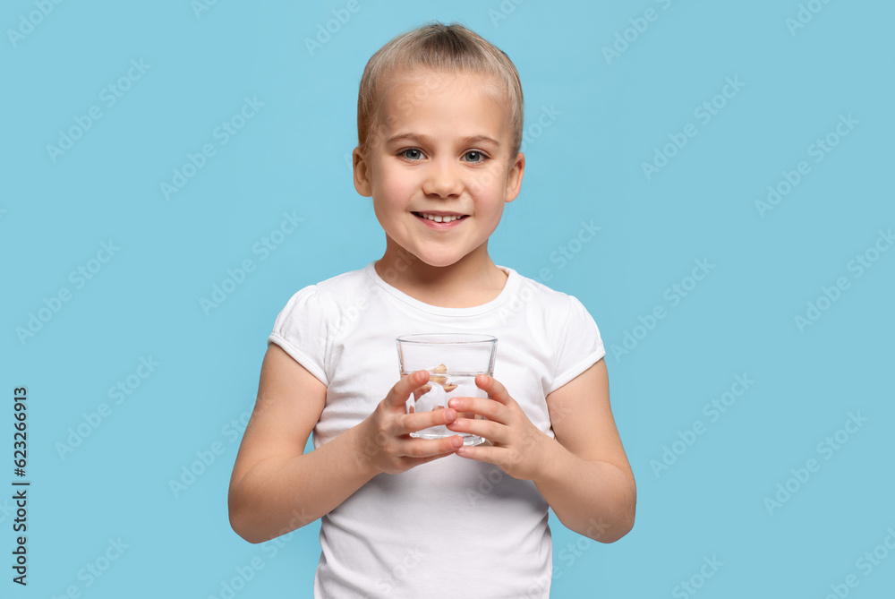 Happy little girl holding glass of fresh water on light blue background, space for text Happy little girl holding glass of fresh water on light blue background, space for text