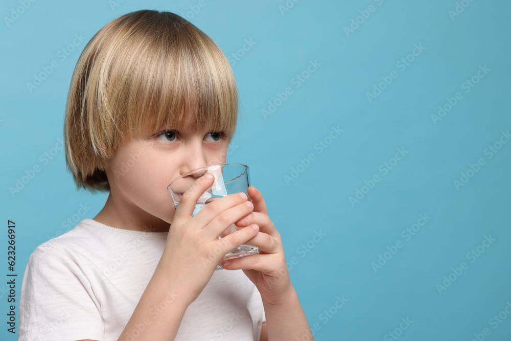 Cute little boy drinking fresh water from glass on light blue background, space for text Cute little boy drinking fresh water from glass on light blue background, space for text