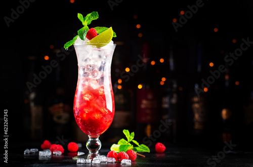 Raspberry lemonade cocktail or mocktail drink with raspberries, syrup, soda, lime, mint and ice, dark bar counter background, copy space