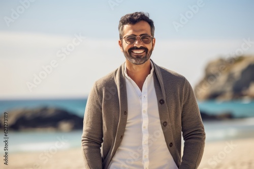 Portrait of handsome man in casual clothes standing on beach and smiling at camera