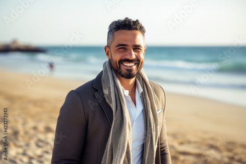 Portrait of a smiling young man in coat and scarf standing on the beach