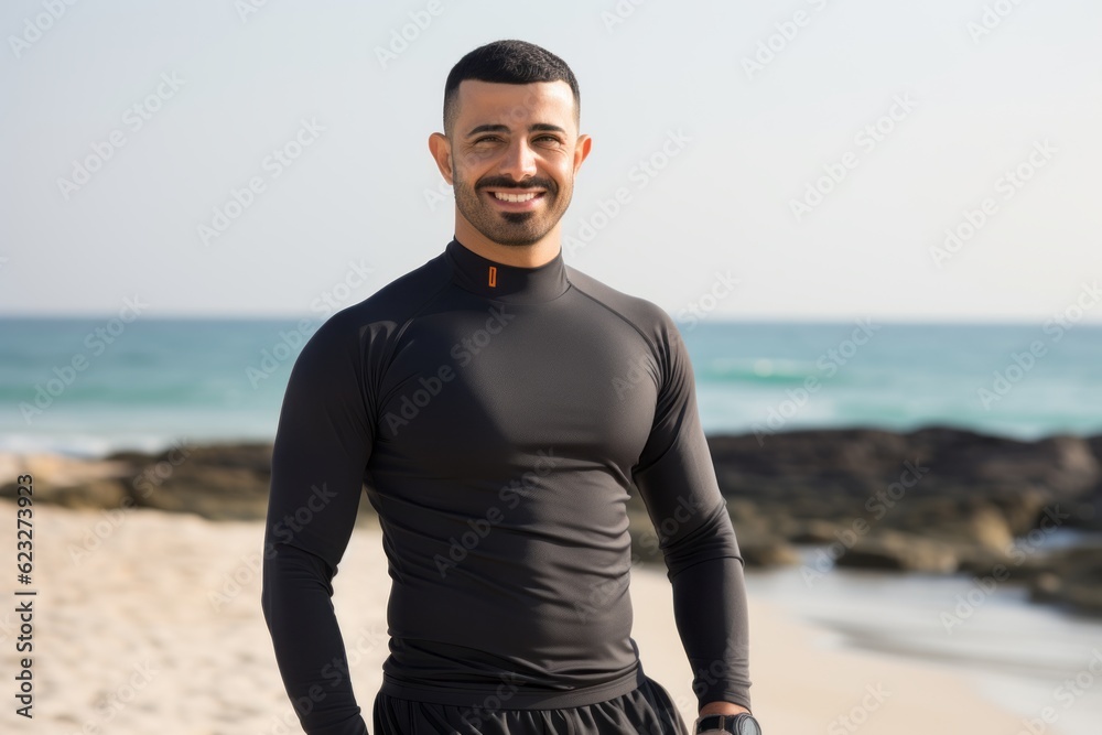 Fototapeta premium Portrait of smiling man in wetsuit standing on sandy beach