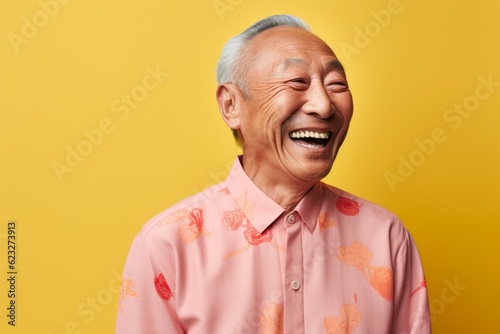Portrait of a happy senior asian man laughing on yellow background © Eber Braun