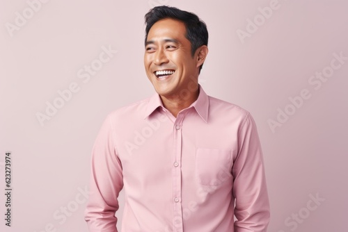 Portrait of a happy young asian man smiling against pink background