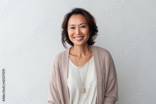 Portrait of a smiling middle-aged Asian woman standing against grey background