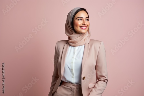 Portrait of a beautiful young asian muslim woman wearing hijab smiling at camera isolated over pink background © Leon Waltz