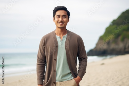 Portrait of smiling young man standing with hands in pockets at beach