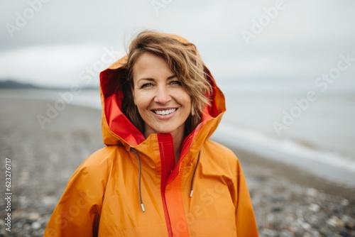 Portrait of smiling woman in raincoat standing on beach and looking at camera © Anne Schaum