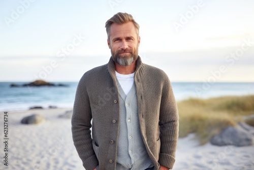 Portrait of handsome mature man standing on beach with hands in pockets