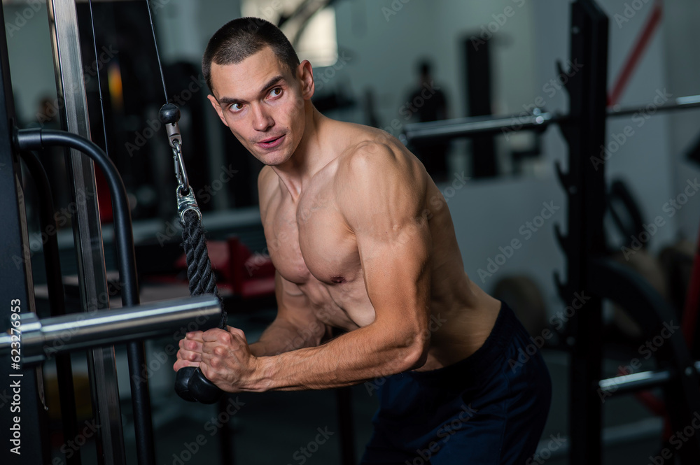 Shirtless man doing triceps pulldown at the gym. 