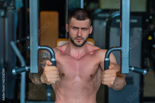 Muscular hunk with posing in gym. Fitness male model near gym equipment. Young muscular man workout. Sport man with strong muscular torso in gym. Sport and motivation. Exercises with weight.