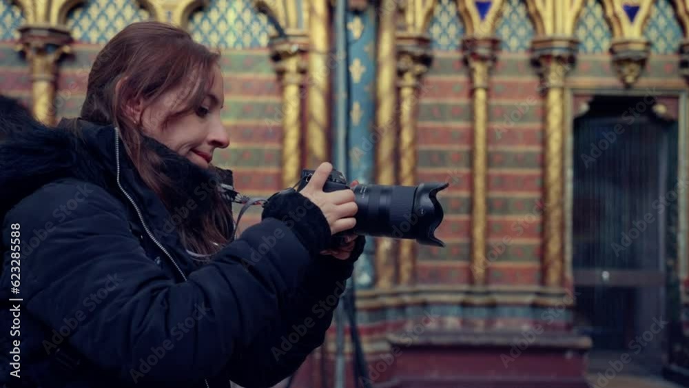 Side view of young Hispanic woman in warm jacket taking photo with professional camera of majestic interior of the Gothic chapel Sainte Chapelle in city of Paris, France