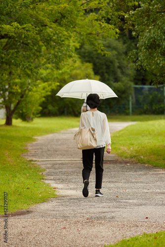 夏の公園で日傘を持って散歩している若い女性の後姿