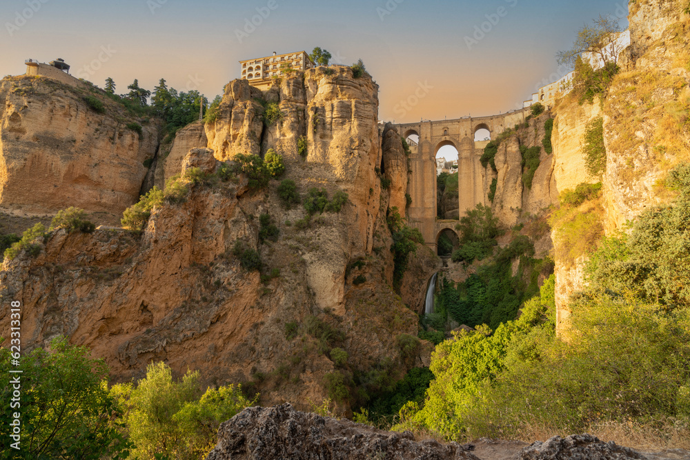 Daytime landscape photo of the Puente Nuevo bridge in Ronda, Andalusia, Spain. The bridge and surrounding cliffs are bathed in golden light.
