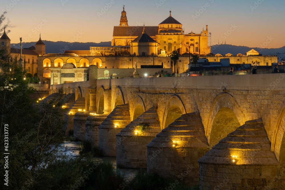Roman bridge of Córdoba at twilight. Bridge and Mezquita mosque are bathed in golden light. Low angle photo, slightly beneath the bridge.