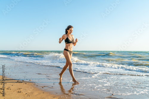 young woman in a black swimsuit posing on a sandy seashore at sunset in summer