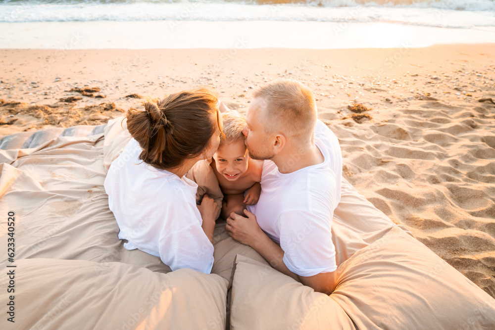 happy family on the beach at sunset lie on a bed on the sand, mom dad and little son. Family and vacation concept