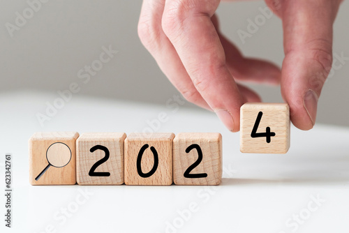 Hand flipping 2023 to 2024 trend year for marketing monitor and business planing change concept.