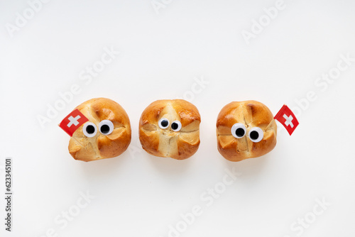 The first august bread buns baked to celebrate national holiday of Switzerland with swiss flag. Funny faces with googly eyes.
