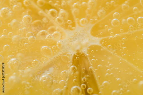 Żółta słoneczna tapeta, soczysta cytryna w szklance z bliska, otoczona bąbelkami wody