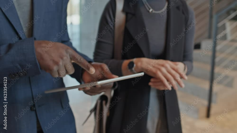 Close-up follow shot of hands of diverse businesspeople discussing presentation on tablet computer, pointing and gesticulating while walking through office lobby on way to work or meeting Close-up follow shot of hands of diverse businesspeople discussing presentation on tablet computer, pointing and gesticulating while walking through office lobby on way to work or meeting