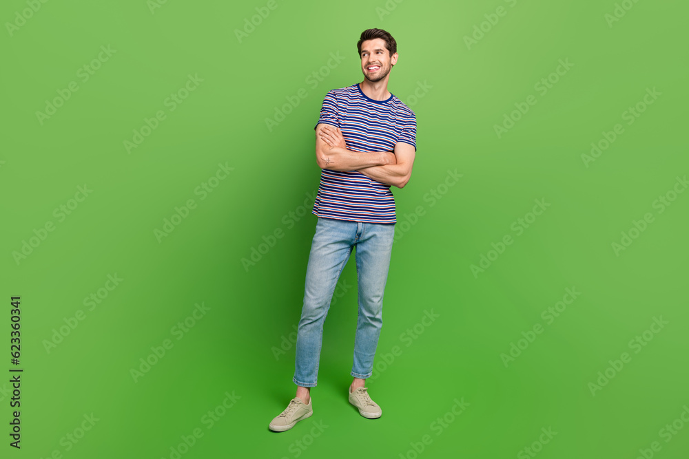 Full length photo of cheerful dreamy man dressed striped t-shirt arm folded looking empty space isolated green color background Full length photo of cheerful dreamy man dressed striped t-shirt arm folded looking empty space isolated green color background