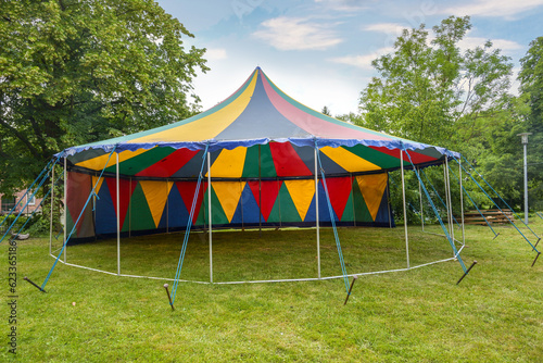 Small colorful circus tent with one pole standing half open on a meadow for a summer party or festival, copy space